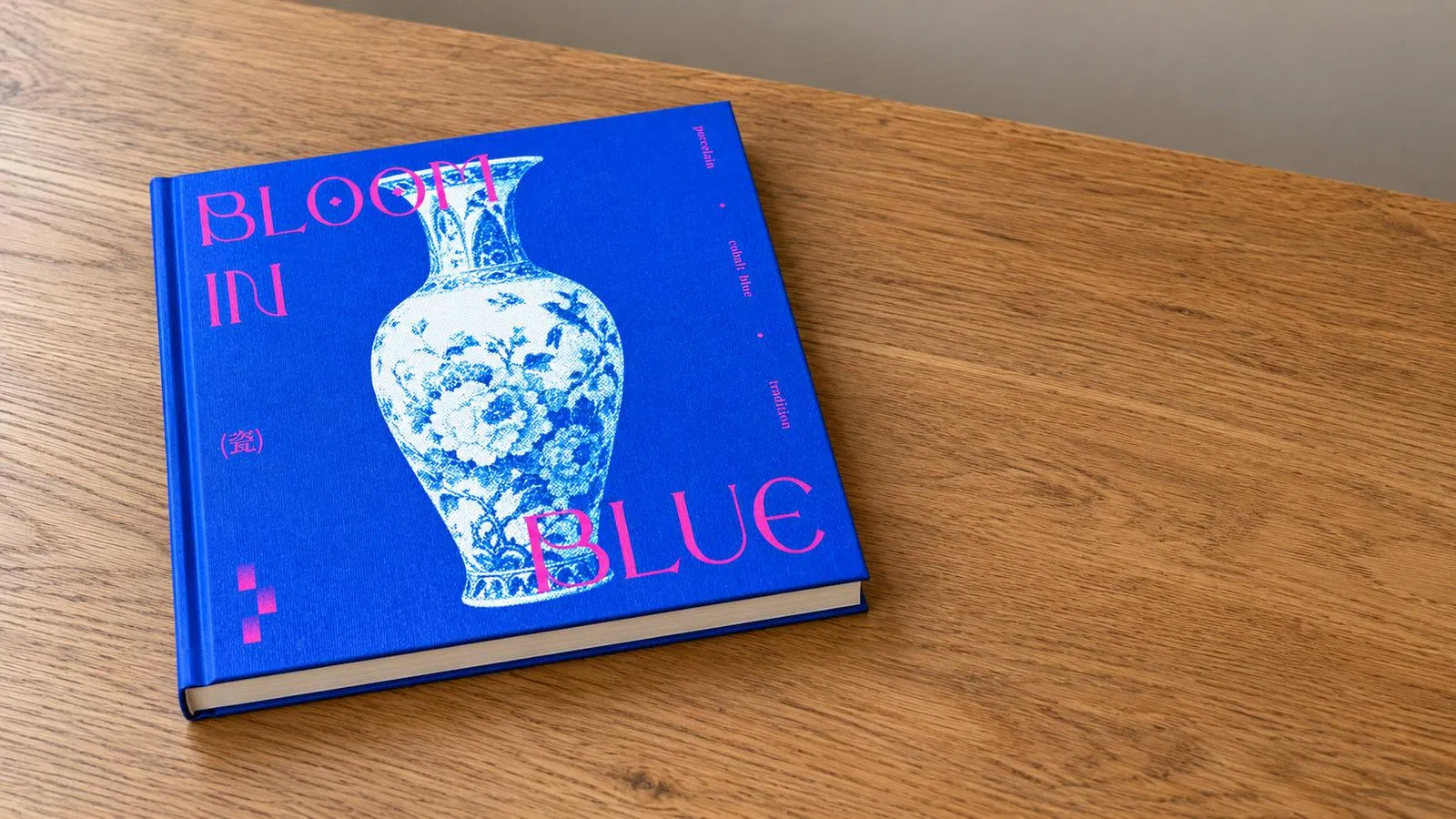 單本精裝書平放在木質桌面，封面使用完整 BLOOM IN BLUE 花瓶作品