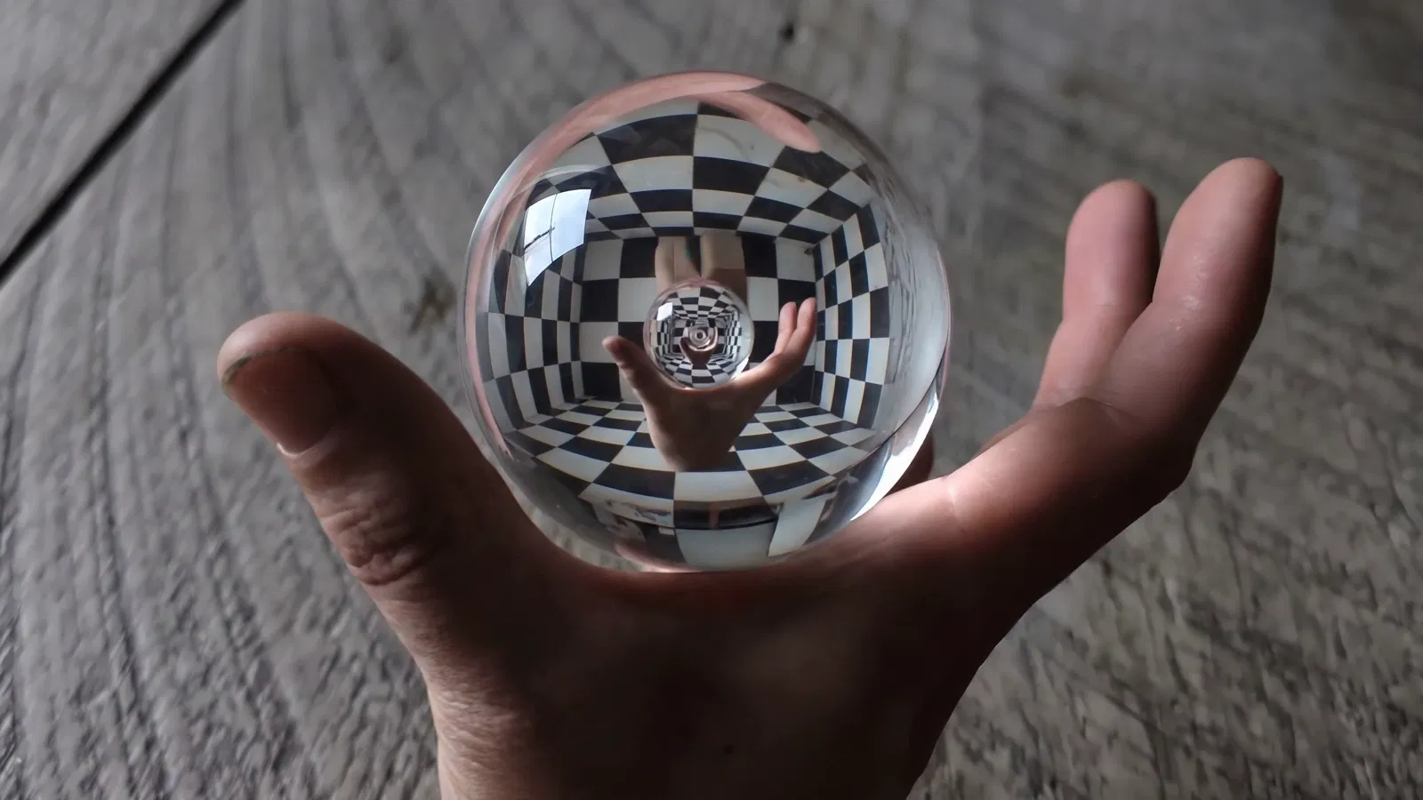 Gemini Omni Flash demo：手掌上的玻璃球，球內是無限遞迴的黑白棋盤房間，房間中央又有同一隻手拿著同一顆球